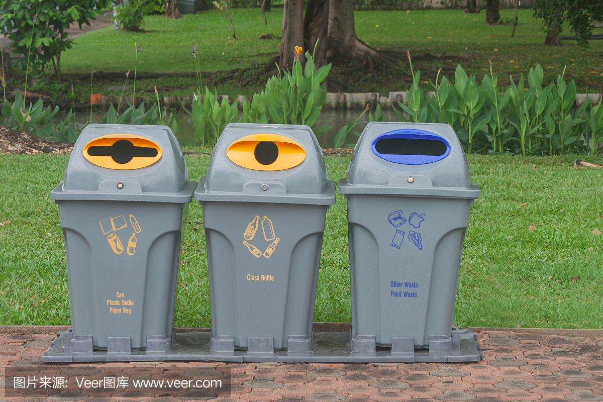 公共回收箱或隔离式回收箱位于公园走道旁的水泥地面上,以绿色自然为背景。(的风格)